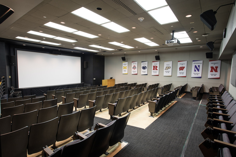 At front, large screen with podium and computer. Facing screen, nine rows of approximately 130 seats total.