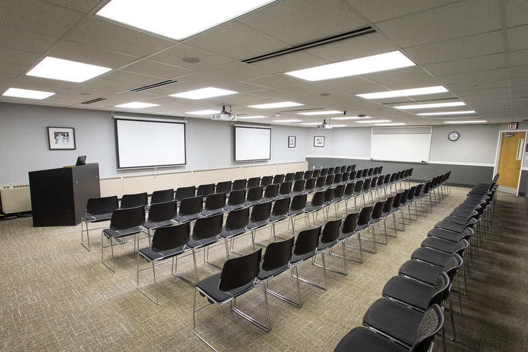 Another alternate angle of five rows of twenty chairs each with a whiteboard, projector, and podium. 