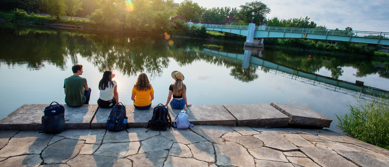 three students sitting along river bank