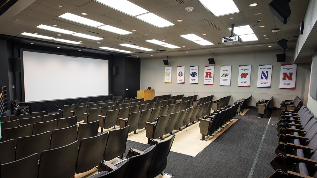 At front, large screen with podium and computer. Facing screen, nine rows of approximately 130 seats total.