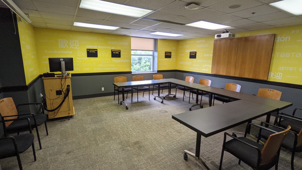 Four tables with a dozen chairs facing a podium with a computer and projector. 