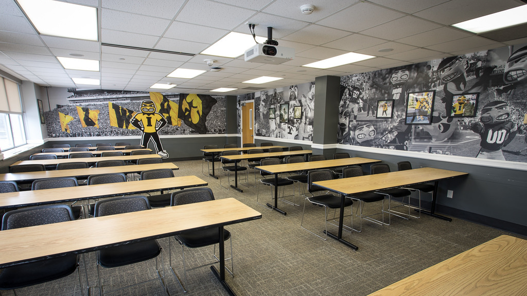 Ten tables with four seats each facing front table, wall displaying photos related to Herky the Hawk. 