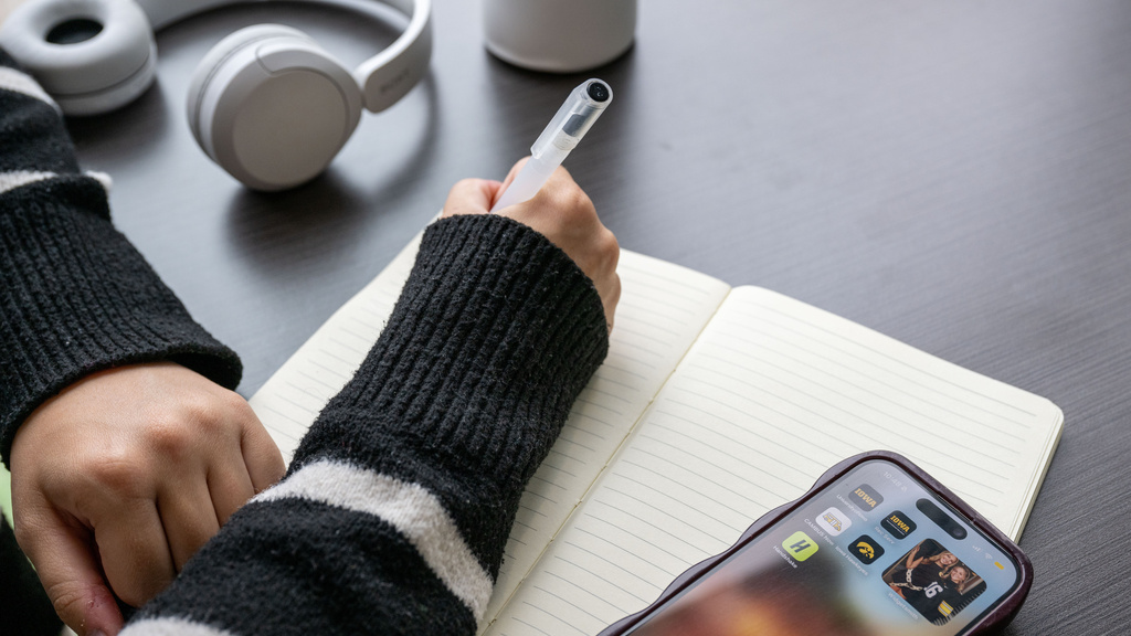 Image of person writing in a notebook with their cell phone nearby and headphones.